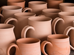 Lori bisque-fired a collection of mugs, varied in size, shape, and design. Next, she will meticulously mask and glaze the mugs in preparation for final glaze firing.